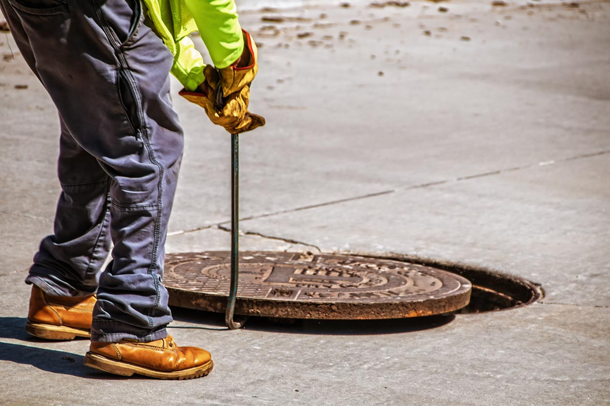 Man removing or replacing a heavy manhole cover in paved street
